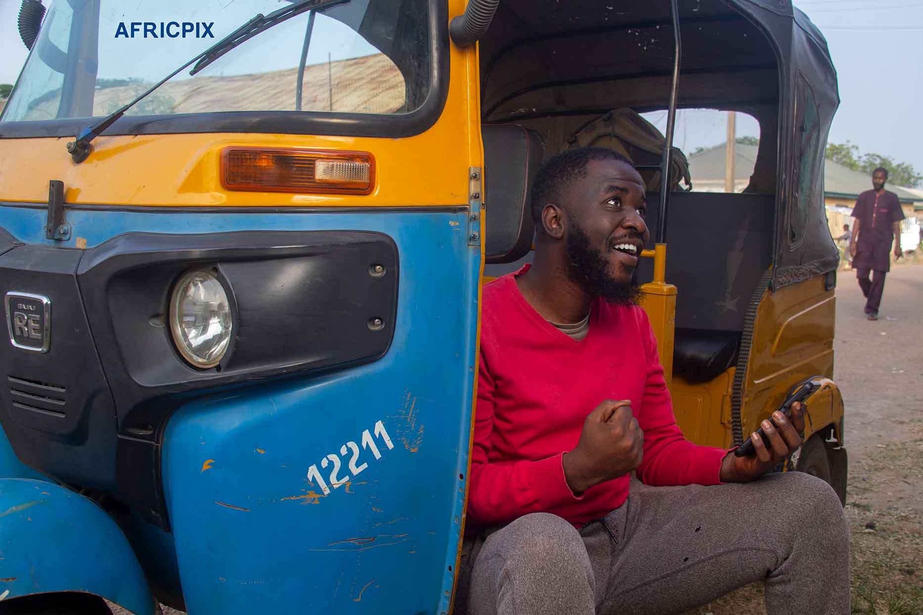 An excited African tricycle rider also known as Keke or Maruwa rider, holding his phone, smiling with joy after receiving good news 3.